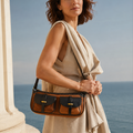 Woman wearing a beige sleeveless dress carrying a Dual-Pocket Full-Grain Leather Crossbody Bag in brown and black with vintage brass hardware by the ocean.