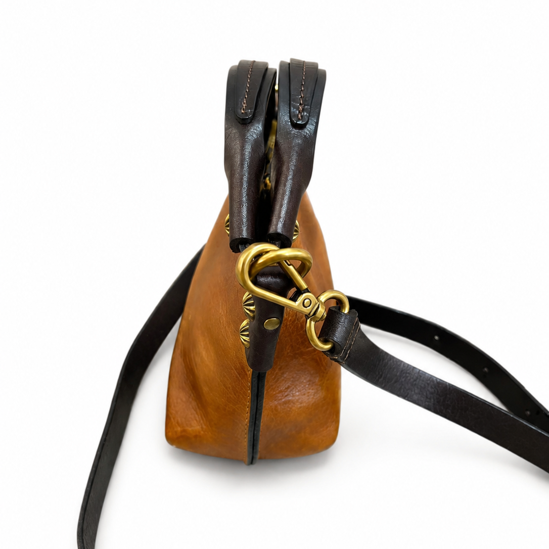 Brown leather bag with black strap and gold clasp on a white background