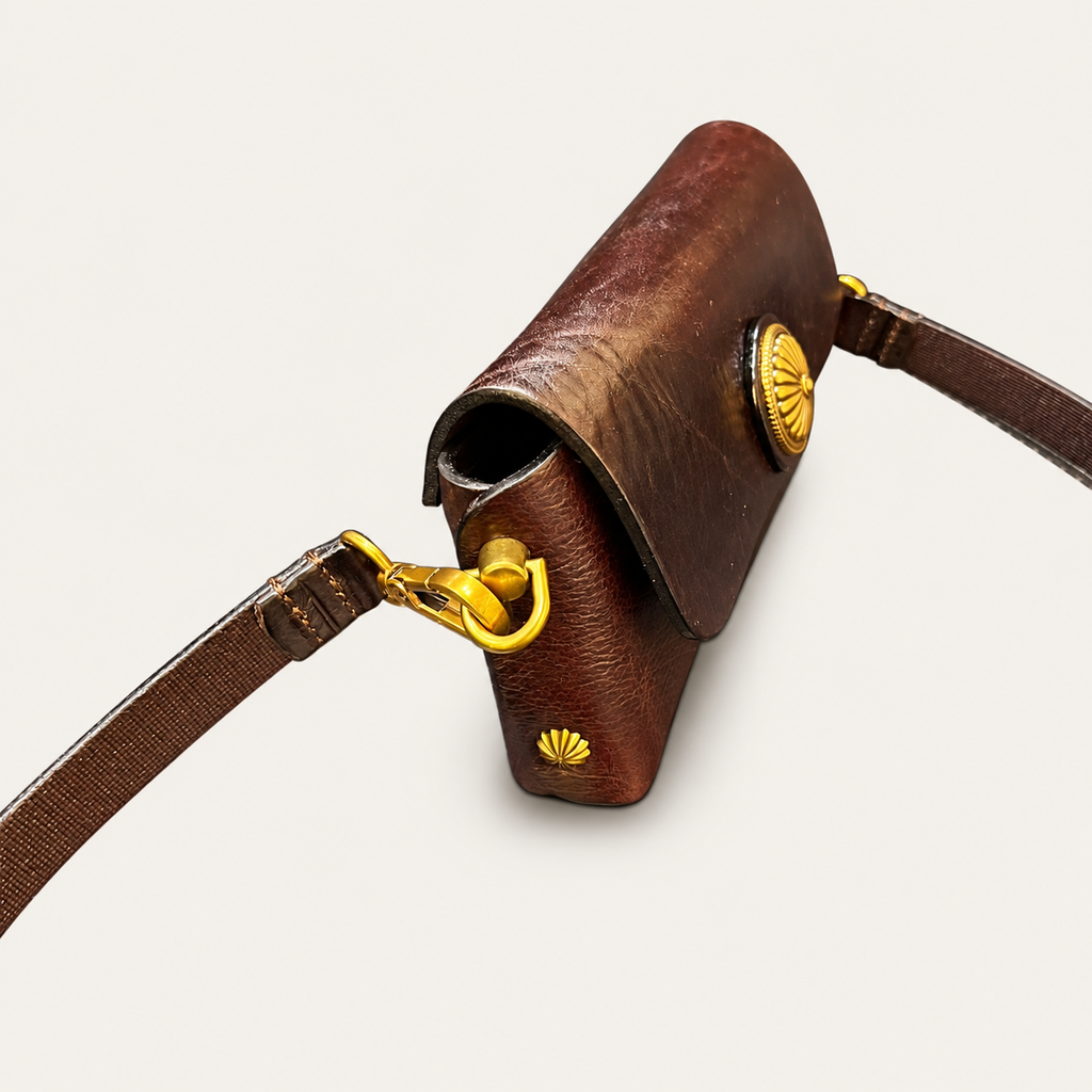 A close-up of a brown leather crossbody bag with gold-tone hardware and a matching leather strap, shown on a light beige background.