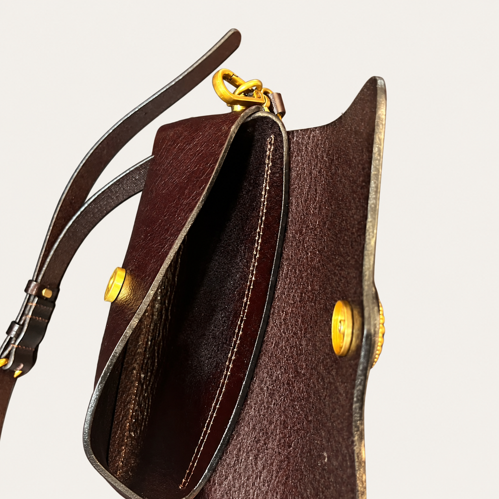 Close-up of a dark brown leather bag with gold-tone hardware and a matching leather strap, shown against a light off-white background.