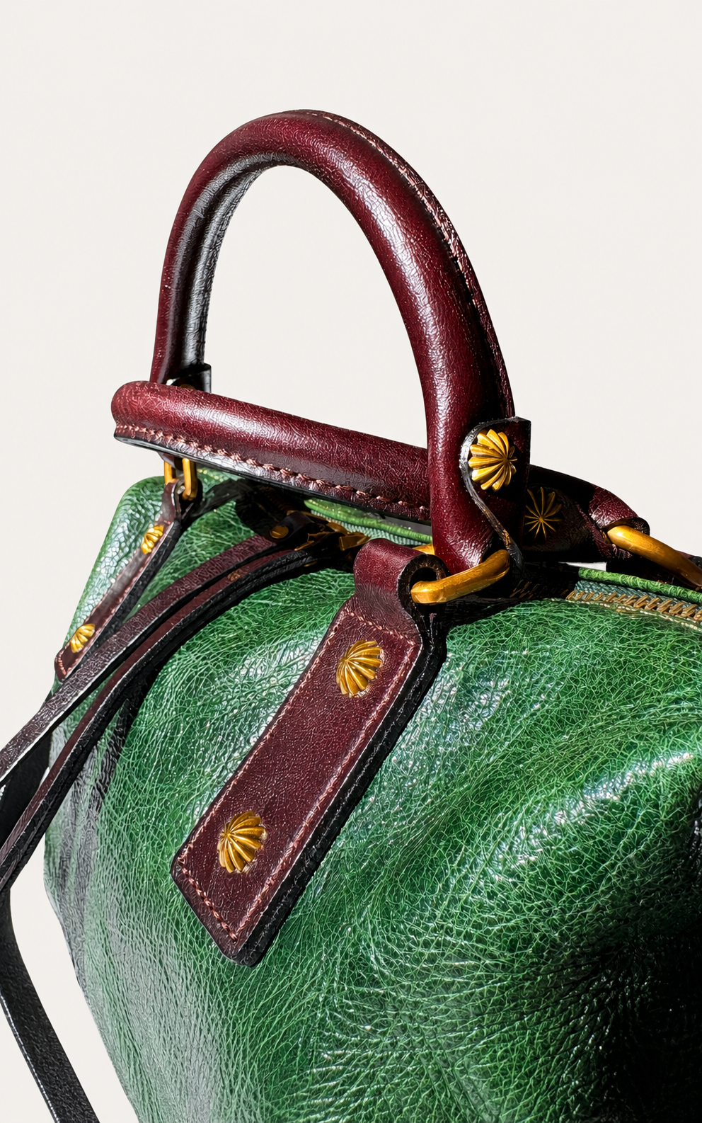 Close-up of a green pebbled leather handbag with dark burgundy leather handles and trim, accented by gold-tone hardware and shell-shaped studs.