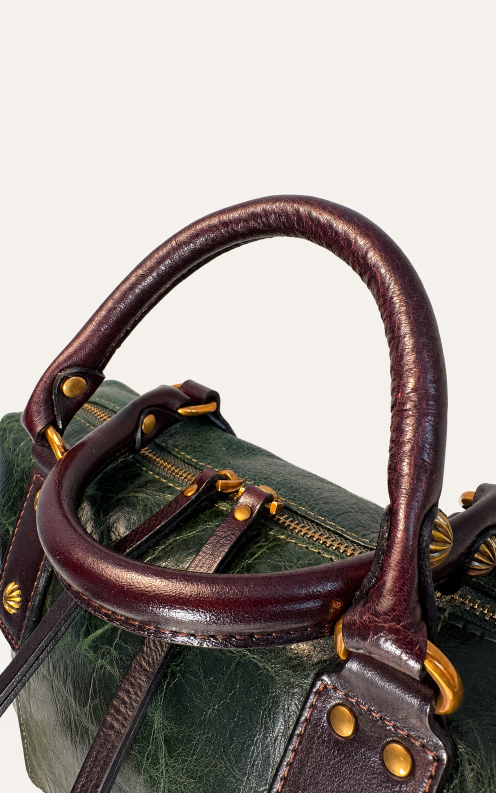 Close-up of a dark green textured leather bag with dark brown leather handles and gold-tone hardware, set against a plain light background.