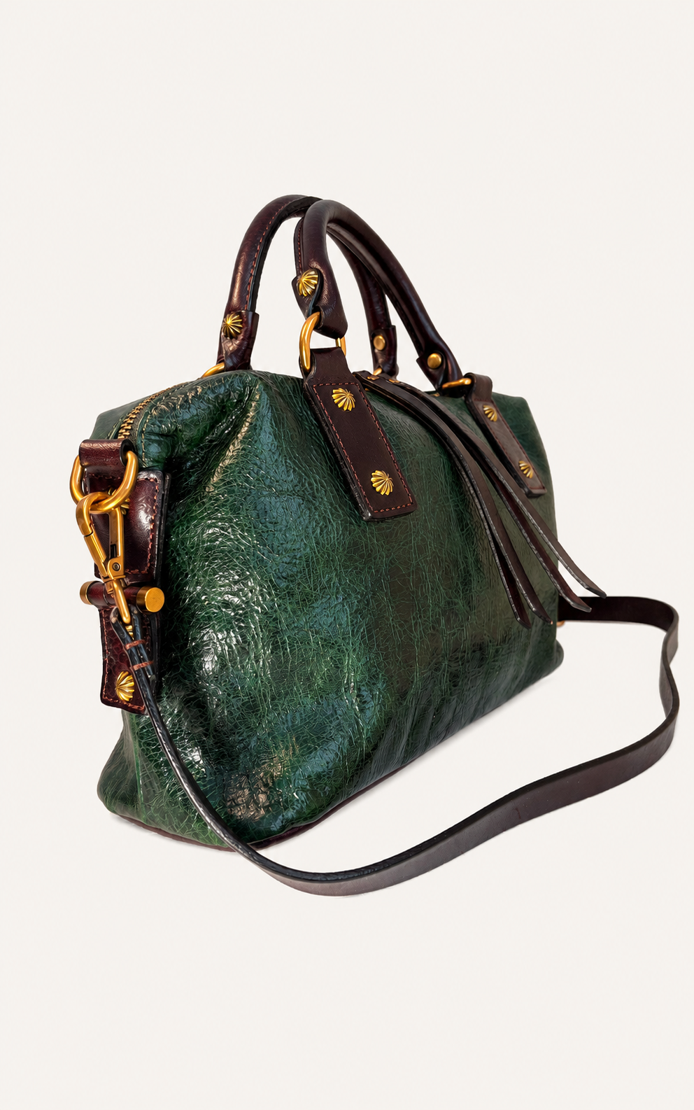 A green textured leather handbag with dark brown leather handles and strap, accented by gold-tone hardware and studs, shown on a light off-white background.