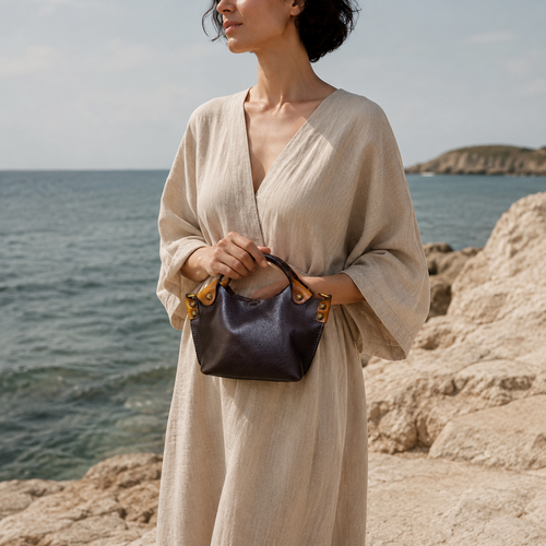 Woman in a beige dress holding a handbag by the ocean