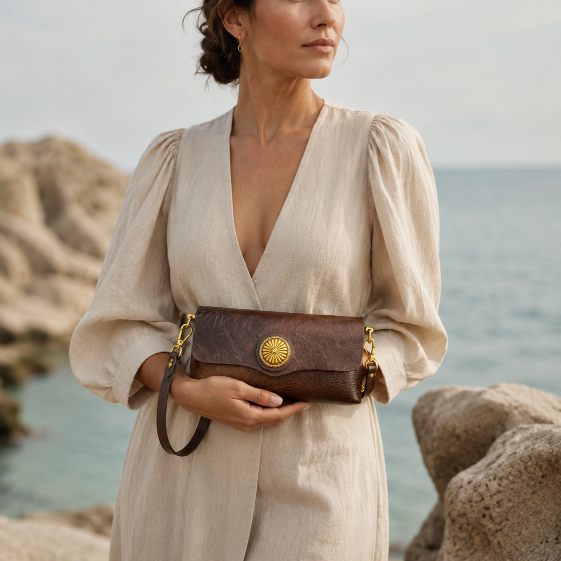 Woman holding a brown leather bag with a gold clasp by the ocean